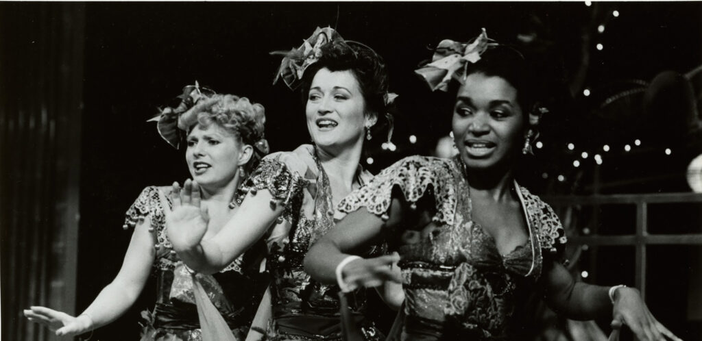 Black and white photograph of three women dressed as chorus girls dancing.