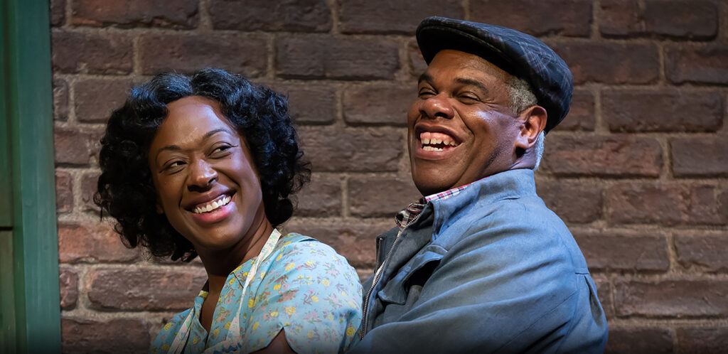 A married couple stands on their porch smiling and embracing.