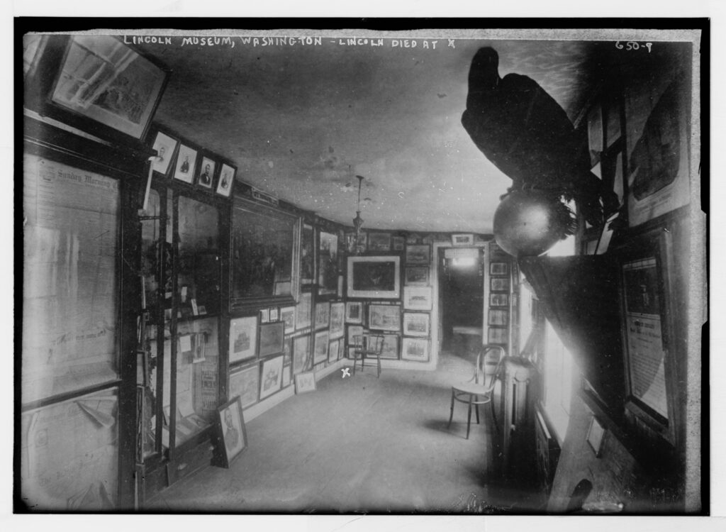 Black and white photograph of a room with the walls covered in framed photographs.