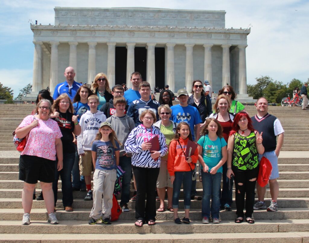 A large group of students stand together on the steps of the Lincoln Memorial.