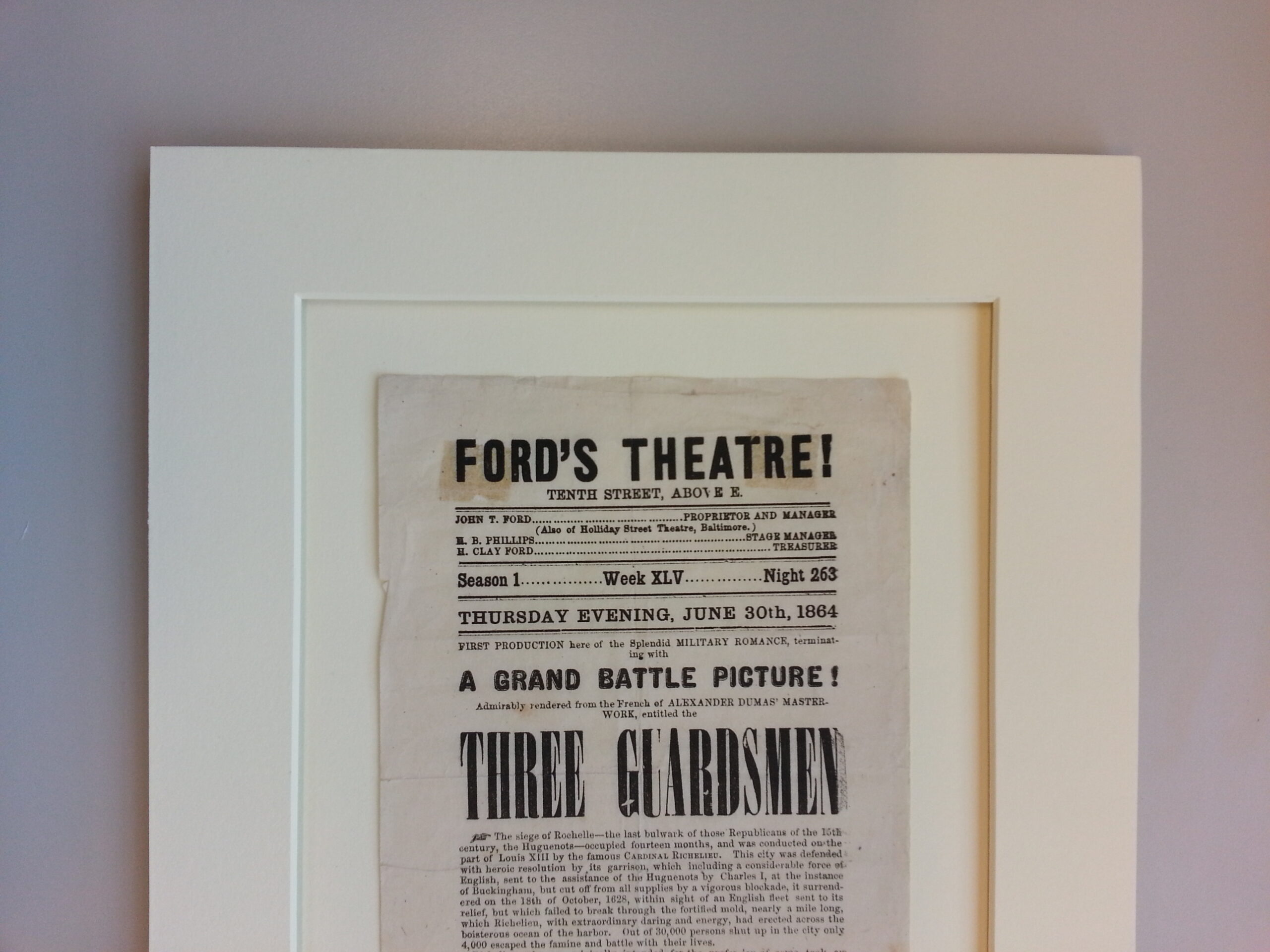 Photograph of mounted Ford's Theatre playbill of <em>Three Guardsman</em>, with printed on paper that has yellowed over time.