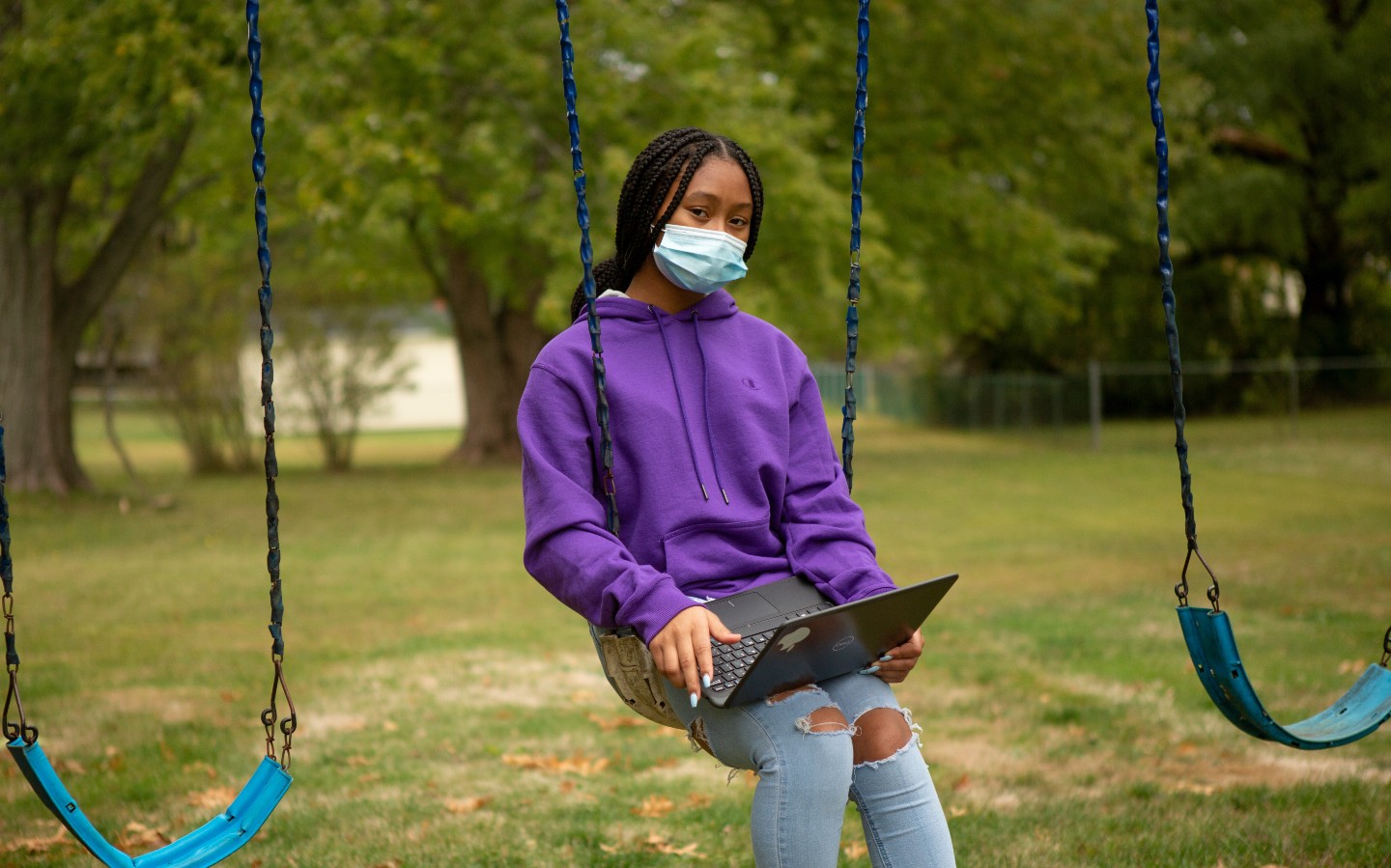 A remote learning student works on an assignment on the swing set at her home.