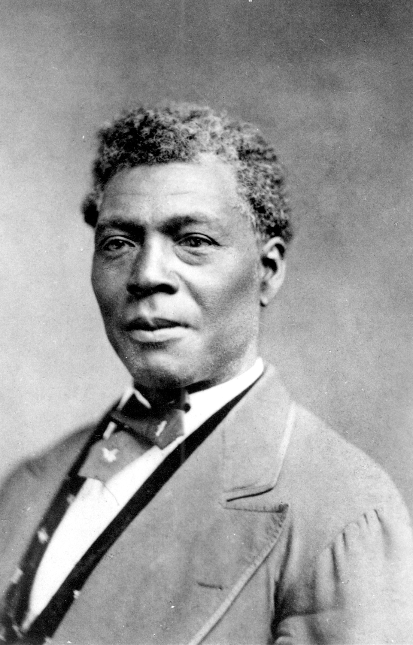 Photograph portrait of Archer Alexander, former slave. Photograph is a copy photo of an earlier work. Alexander is seen from chest up with body and head slightly angled toward the left. He is wearing a light colored jacket with pointed lapel, a dark vest, white shirt, and dark tie.