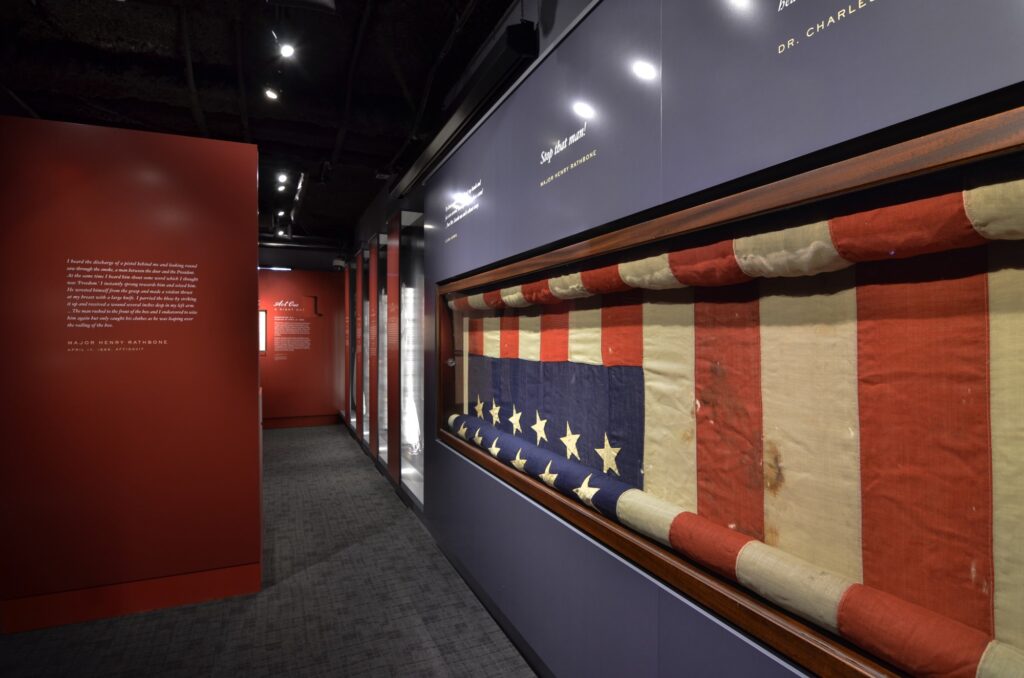 Photograph of a partially rolled up American flag in a blue display case at a museum exhibit.