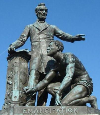Statue in a park features President Abraham Lincoln with the Emancipation Proclamation in his right hand and holding his left hand over the head of a liberated slave kneeling at his feet.