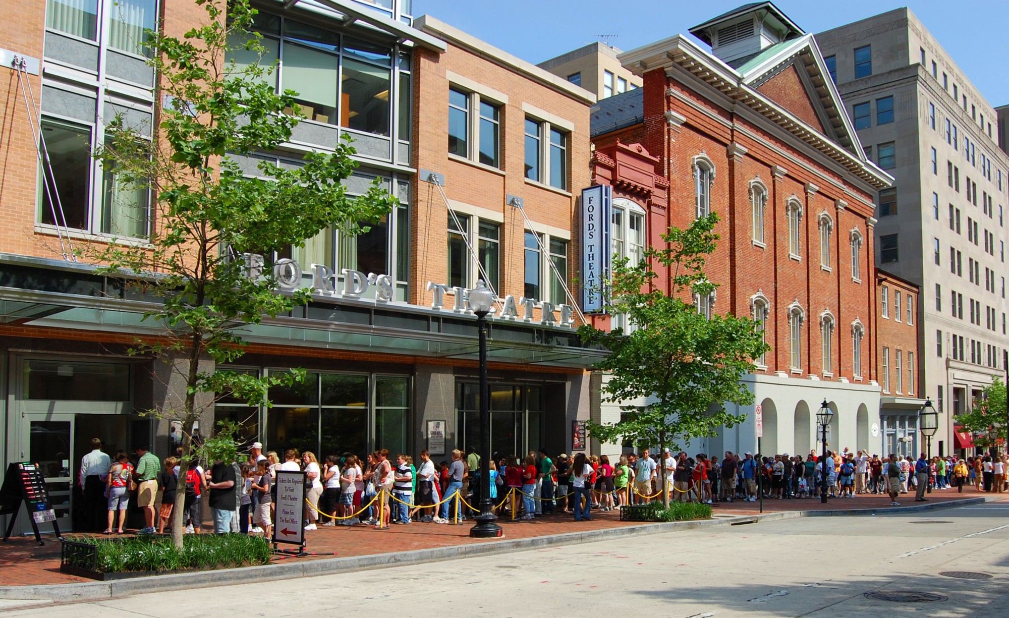 Exterior of Ford's Theatre on a sunny day. A line of patrons stretches across the lobby and historic theatre.