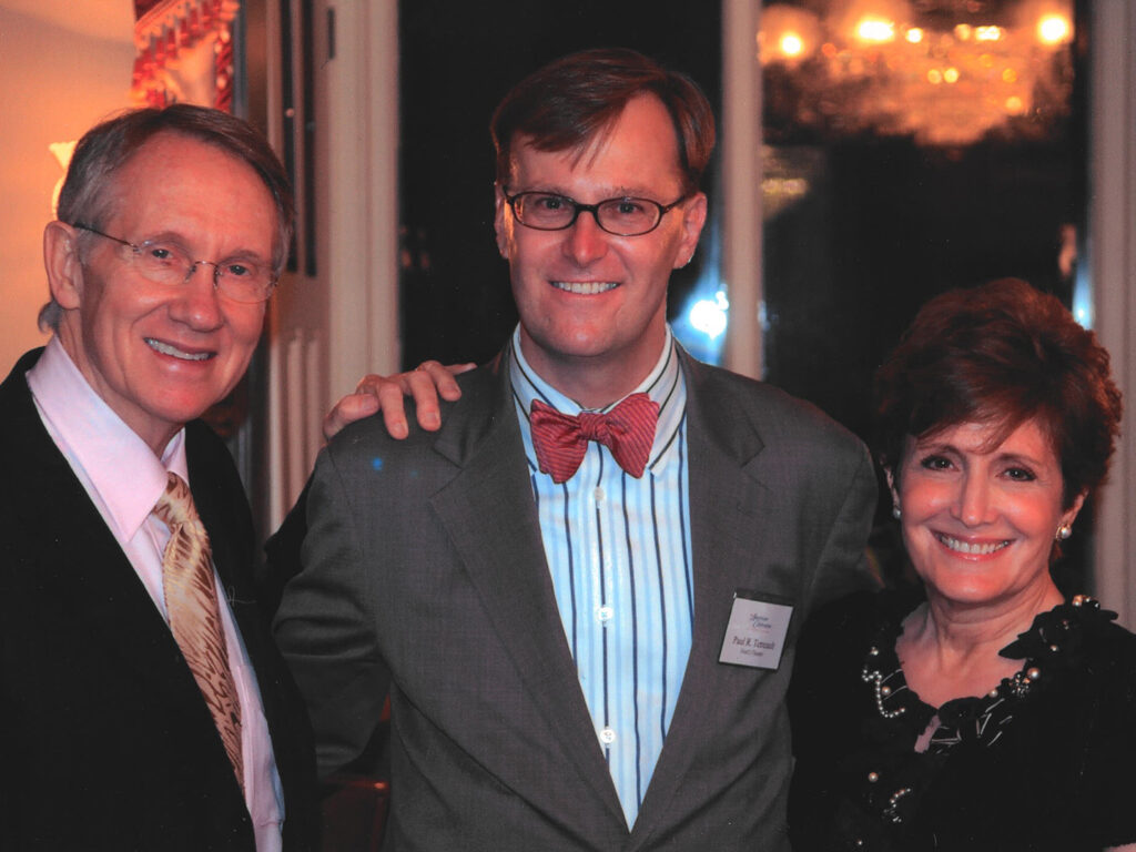 Senator Harry Reid, Ford's Theatre Director Paul Tetreault, and Landra Reid standing arm in arm in a decorated hallway.