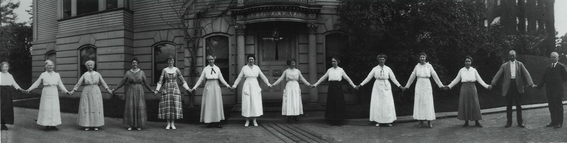1918 black-and-white photograph of the Harvard "computers" holding hands and standing in a line like paperdolls.