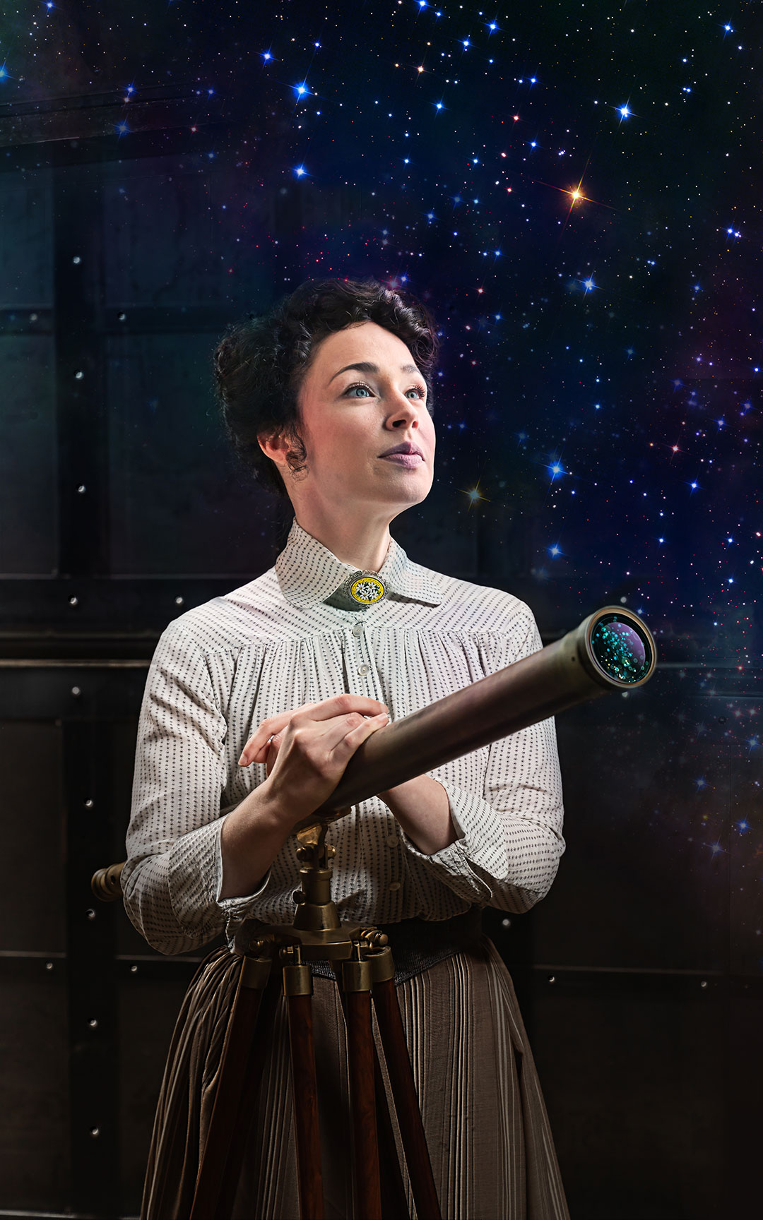 A woman wearing a white, collared Victorian blouse and high-waisted skirt stands behind a telescope looking wistfully into the sky.