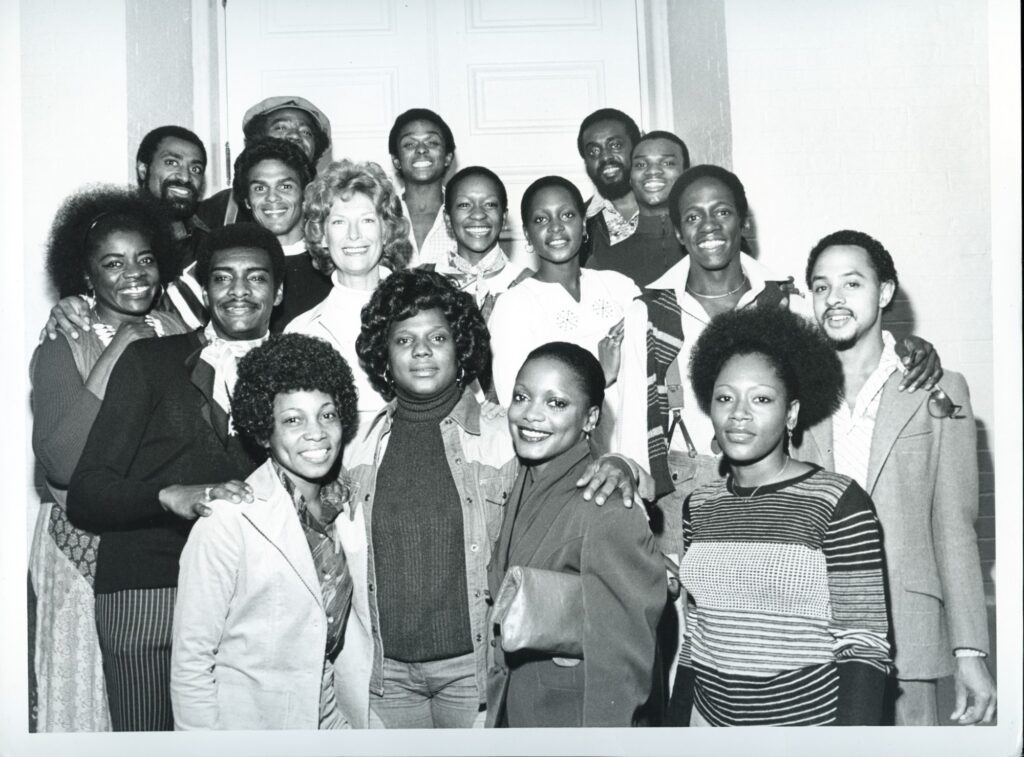 A black and white photograph of a group of men and women dressed in 70's style clothing.