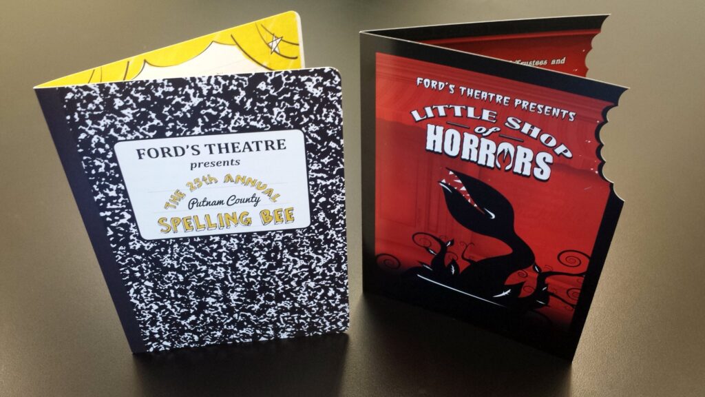 Photograph of two booklets standing upright on a table. One says "Little Shop of Horrors." The other says "25th Annual Putnam County Spelling Bee."