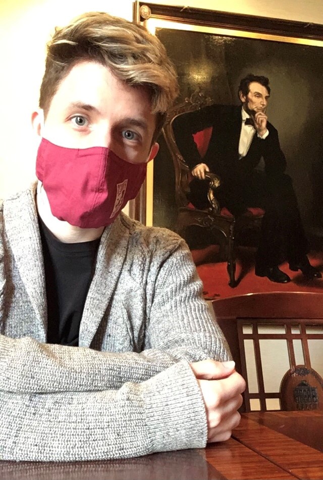 Jacob stands with arms crossed in front of a painting of Abraham Lincoln. 
