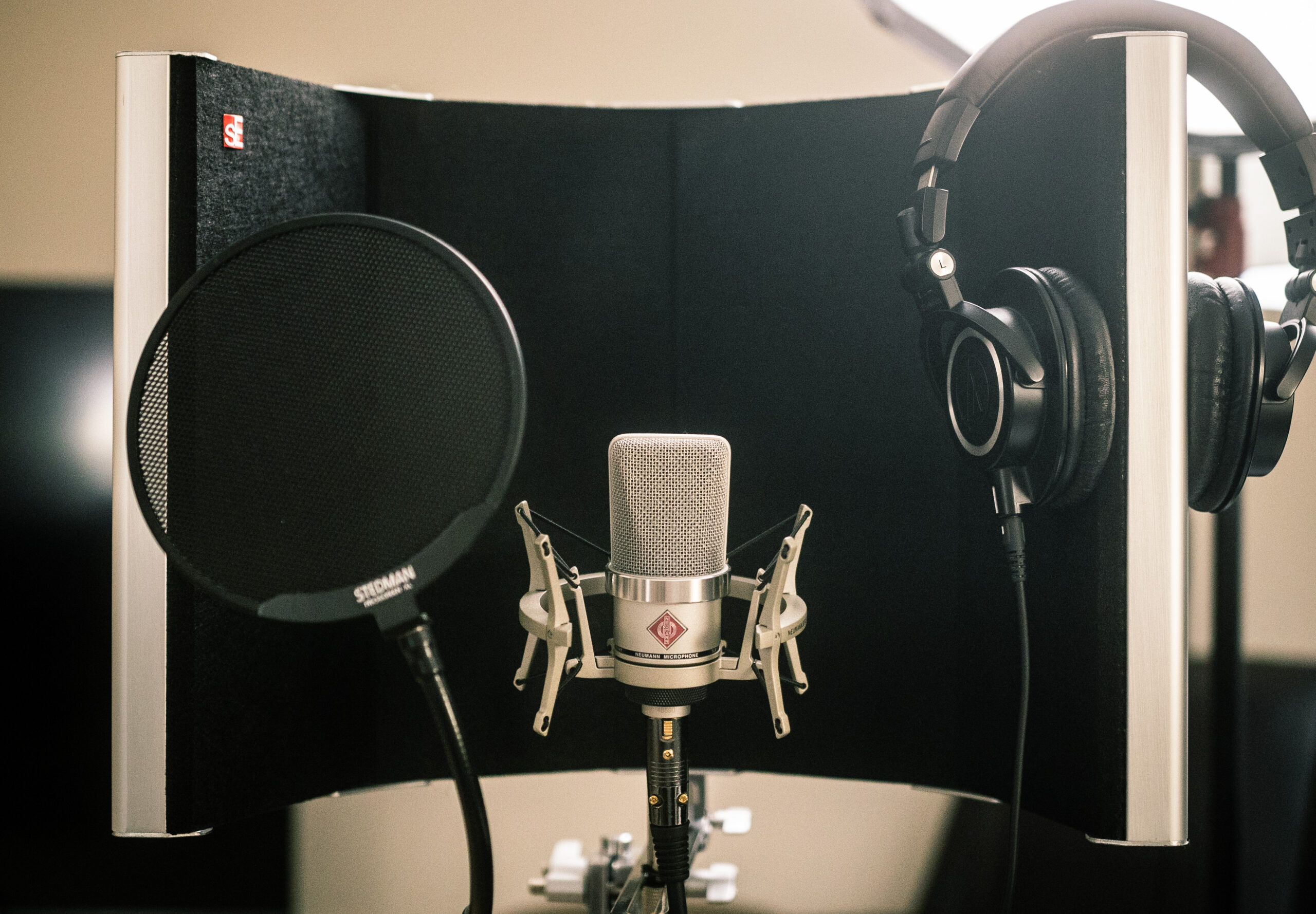A professional recording microphone sits between a pair of headphones and a sound baffle in a recording booth.
