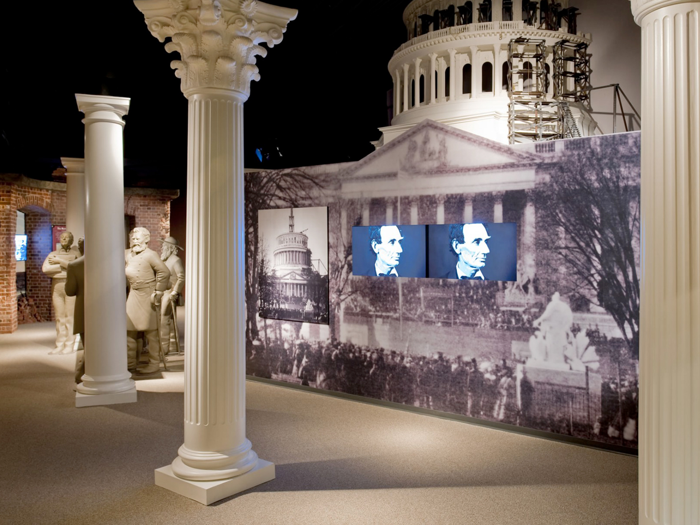Inside the Ford’s Theatre Museum, two television screens display close-up images of Abraham Lincoln’s face. The screens are embedded in a display that is a large-scale photograph of the partially constructed U.S. Capitol dome taken during the Civil War. In front of the display are three white columns, designed to evoke the Capitol. Behind the display is a model of the partially constructed dome.