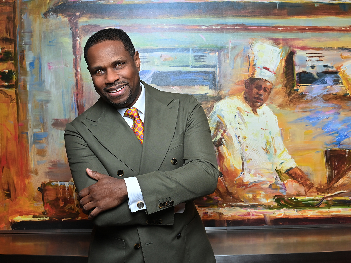 Headshot of Nolan Williams, Jr., standing in front of a painting of a chef.