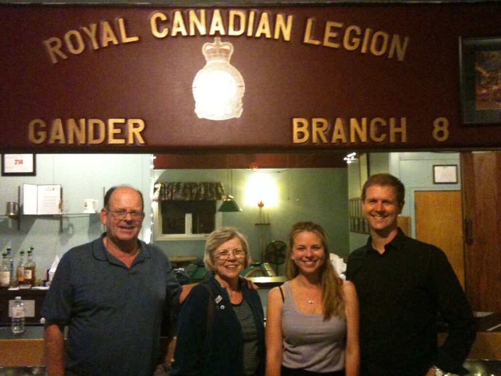 Two men and two women stand in a room in front of a sign that says "Royal Canadian Legion, Gander Branch."
