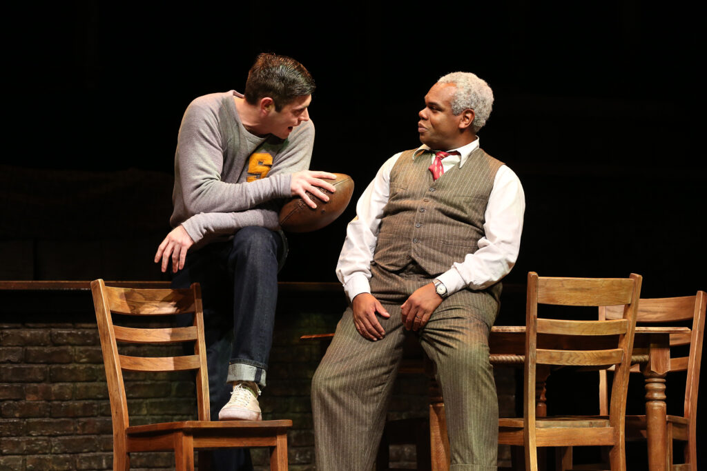 At right, a father in a suit looks proudly at his grown son, who wears a letter sweater and carries a football.