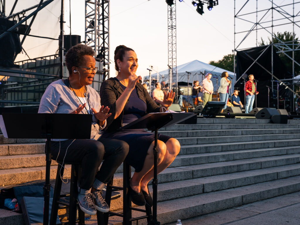 Two ASL interpreters sit on stools near the Come From Away: In Concert at the Lincoln Memorial stage.