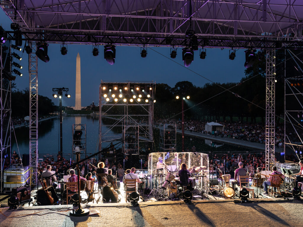 At dusk, thousands of people sit along the north and south sides of the Reflecting Pool while the concert plays on the outdoor stage.