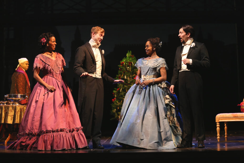 A woman in a formal dress made of mauve taffeta laughs as a man in black-and-white formal attire tells a story. Another woman in a formal dress made of blue taffeta and another man in black-and-white formal attire look on.