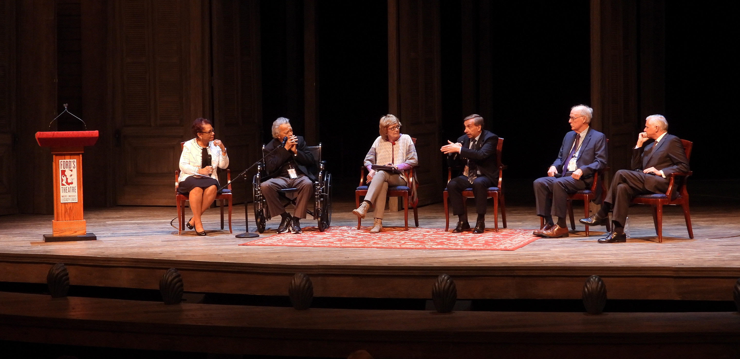 Six people sit on a stage and have a discussion.