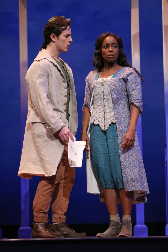 A man dressed in a plain tan linen coat pleased with his former lover, a woman who was previously enslaved. He holds a letter. She looks mournfully away from him. She wears an 18th-century-style purple dress with yellow flowers over casual contemporary blue capris.