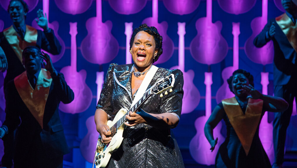Image of African American woman playing a white guitar in sparkly dress.