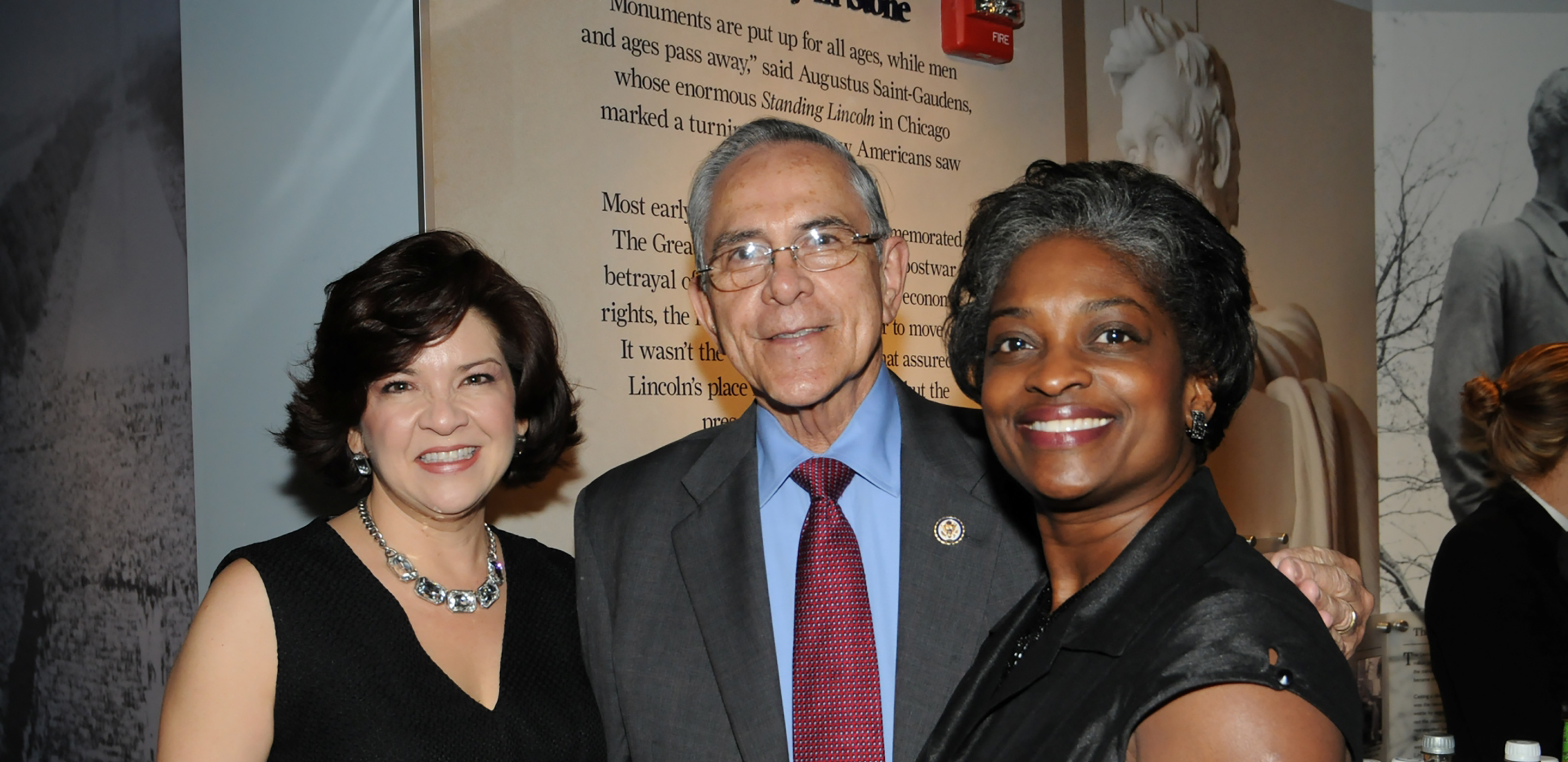 Two woman and a man pose together at a reception in the Center for Education and Leadership.