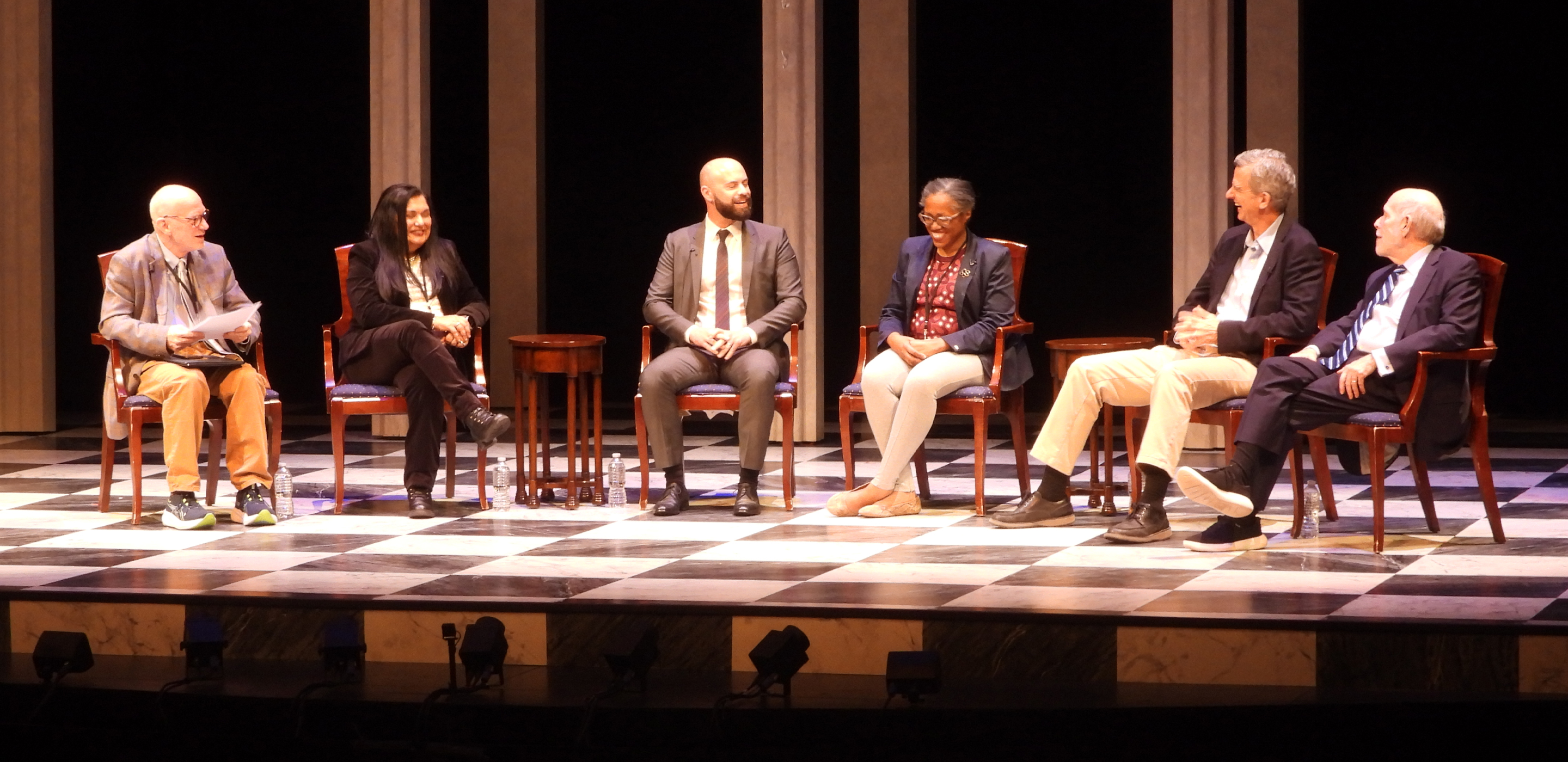 Six panelists sit on a stage and have a discussion.