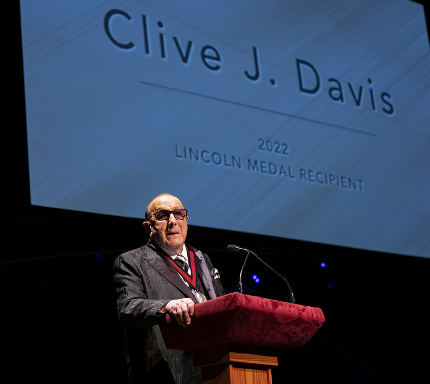 Clive Davis giving a speech at a podium in front of a projection reading, “Clive J. Davis. 2022 Lincoln Medal Recipient.”
