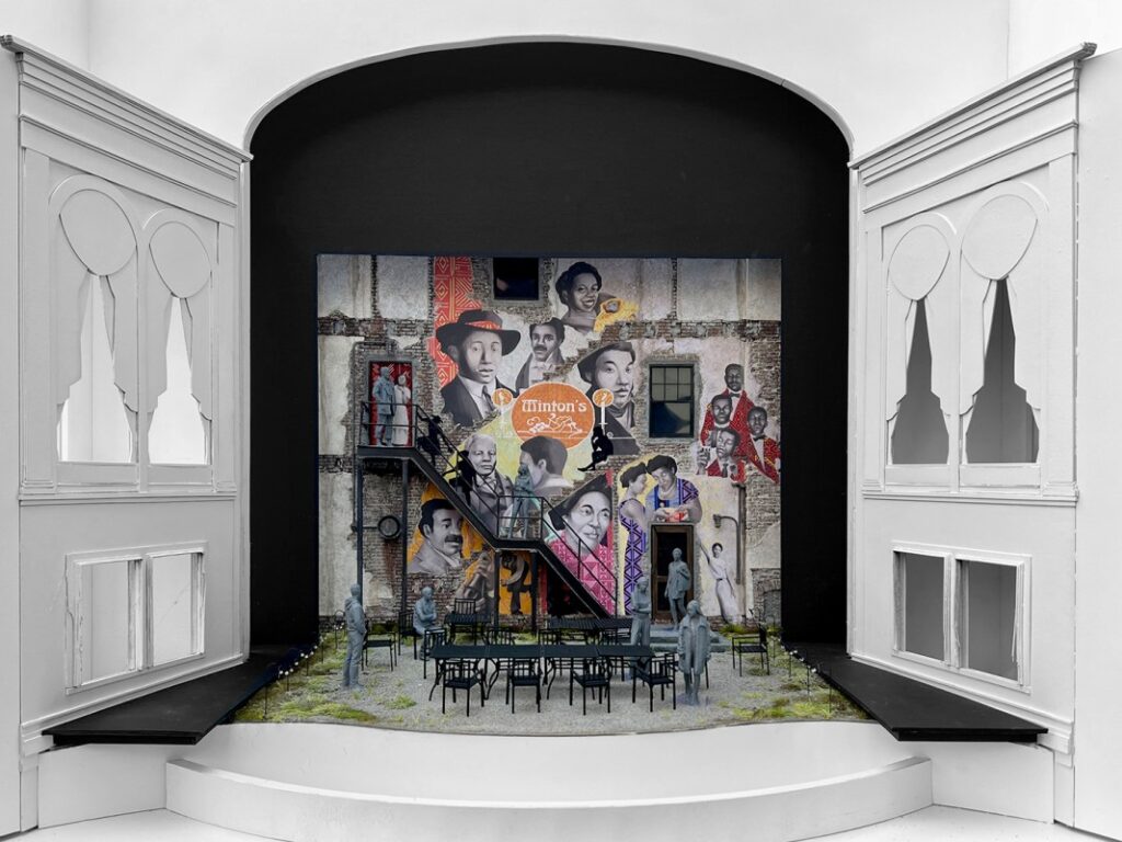 Wide view of the "Grace" set model showing the Ford's Theatre boxes on either side of the stage. Set features a grey-brick row house painted with a three-story mural. In the courtyard below are arranged several rectangular tables and chairs.