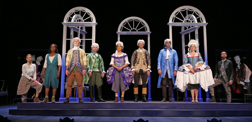 Nine actors stand on a raised platform in a line. Six of them are dressed in ostentatious 18th-century clothing and wigs made of paper. The other three wear more casual clothing inspired by the 18th-century. Behind them are white arched frames, representing mansion windows and doors.