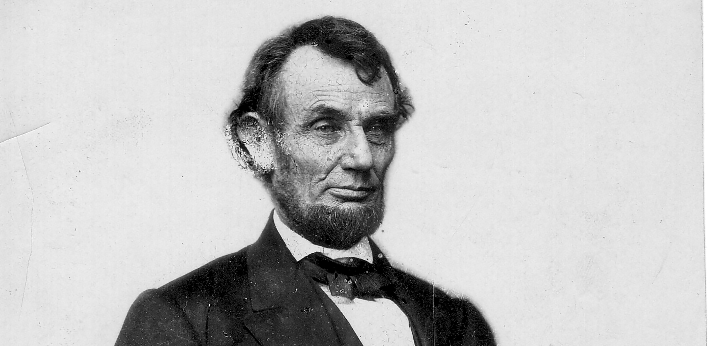 Abraham Lincoln, wearing his signature beard and dressed in a suit, is seated for a formal portrait. He looks off to his left. He is photographed from the legs up.