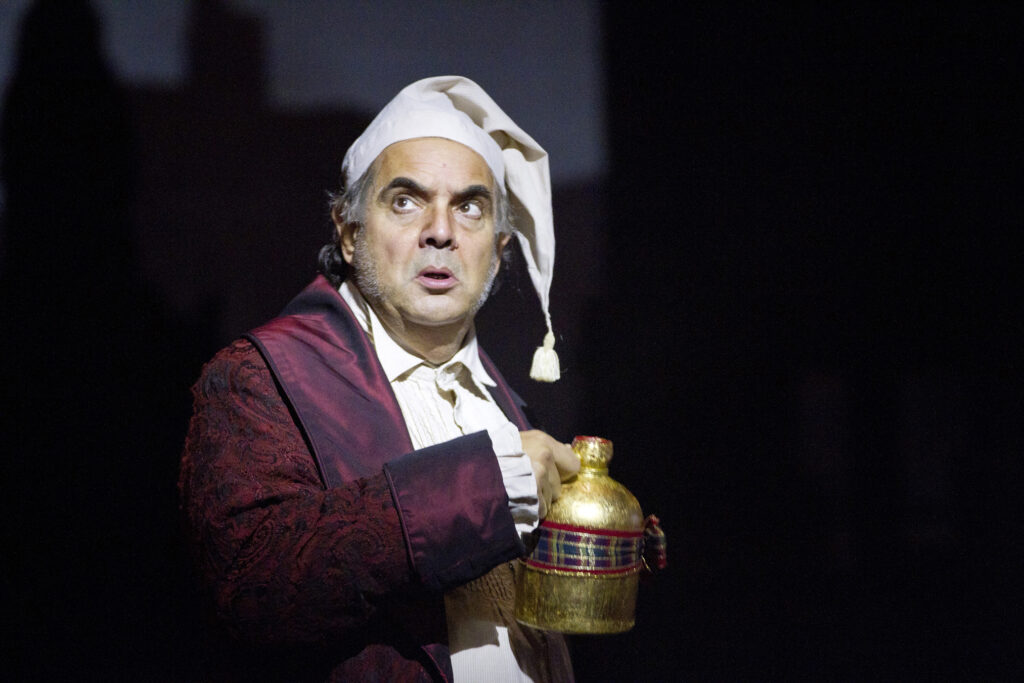 A man in Victorian nightclothes holding a golden jug and looking off-stage.