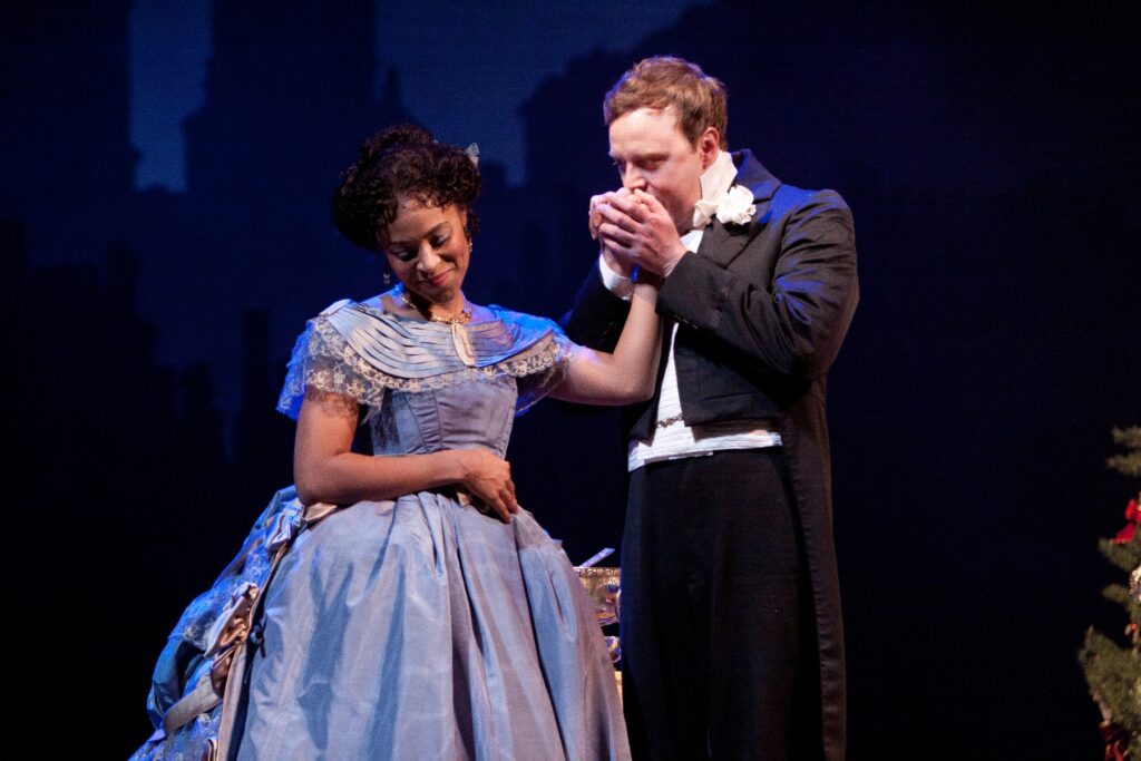 A woman in a long purple dress holds up her hand to be kissed by a man in a tuxedo.