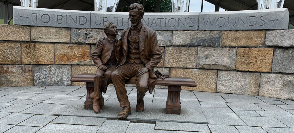 Bronze statue of man and boy sitting on a bench. Behind them is a quotation, “To bind up the nation’s wounds.”
