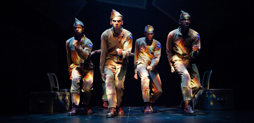 Four African-American men in khaki miliary uniforms sing and dance on a mostly dark stage.