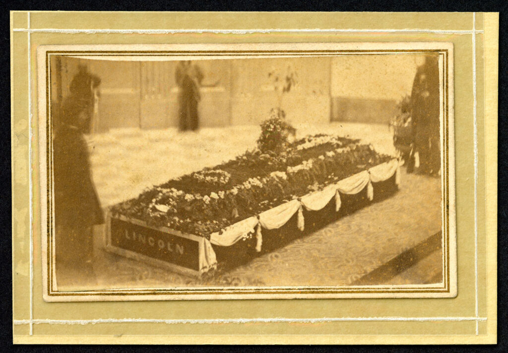 Framed sepia photograph of a catafalque covered in flowers, with "Lincoln" written on the side