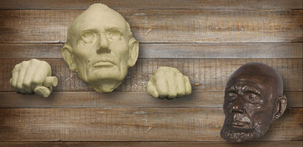 Two plaster casts of the face of Abraham Lincoln, one white and one brown. The white mask also has plaster casts of his hands on either side.