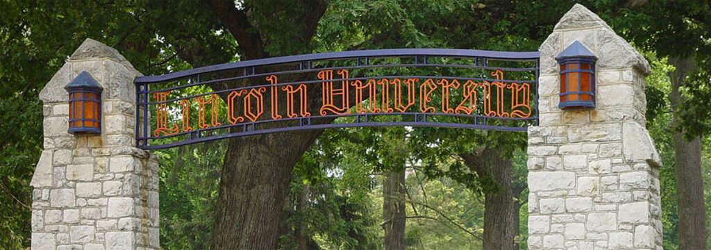 Metal archway with gothic lettering saying “Lincoln University,” with a stone and mortar column on each side.