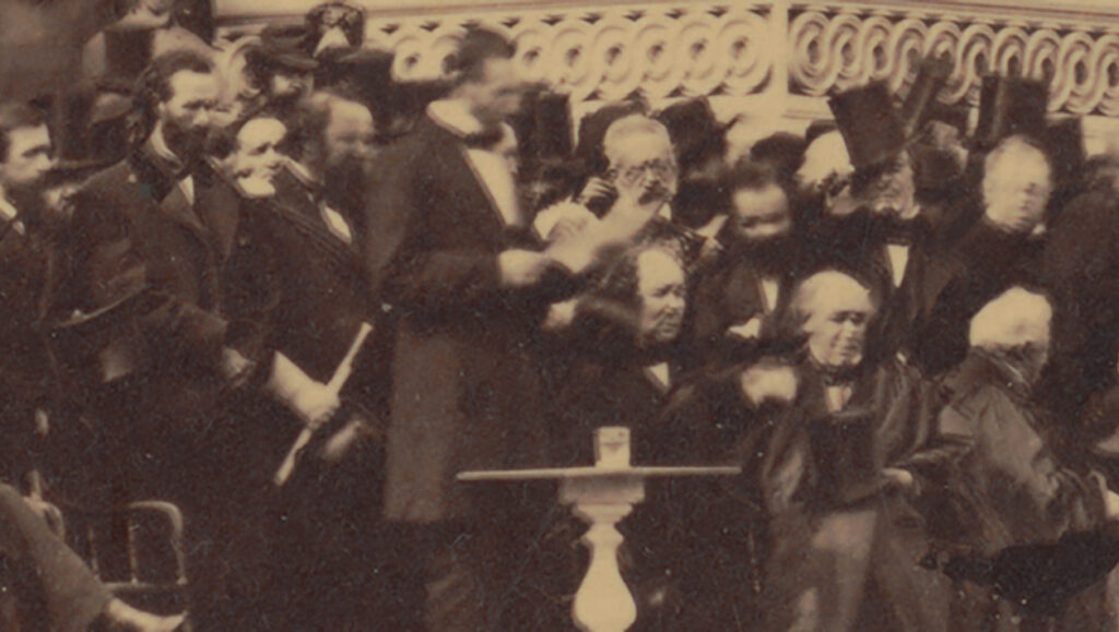 Blurry photograph of Abraham Lincoln giving a speech surrounded by men in suits.
