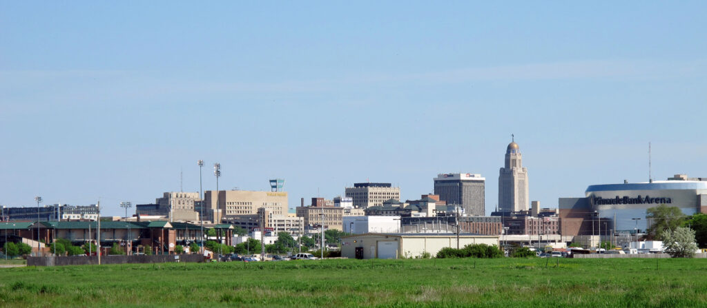 An open field with a city skyline of several multi-story buildings in the background.