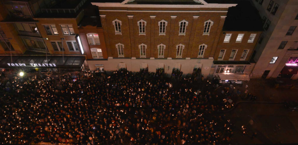 Bird's-eye view photograph of a large crowd gathered on 10th street in front of Ford's Theatre. Many people hold candles.