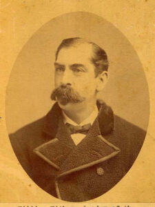 Sepia photograph of a man with a thick mustache and a goatee wearing a heavy overcoat.