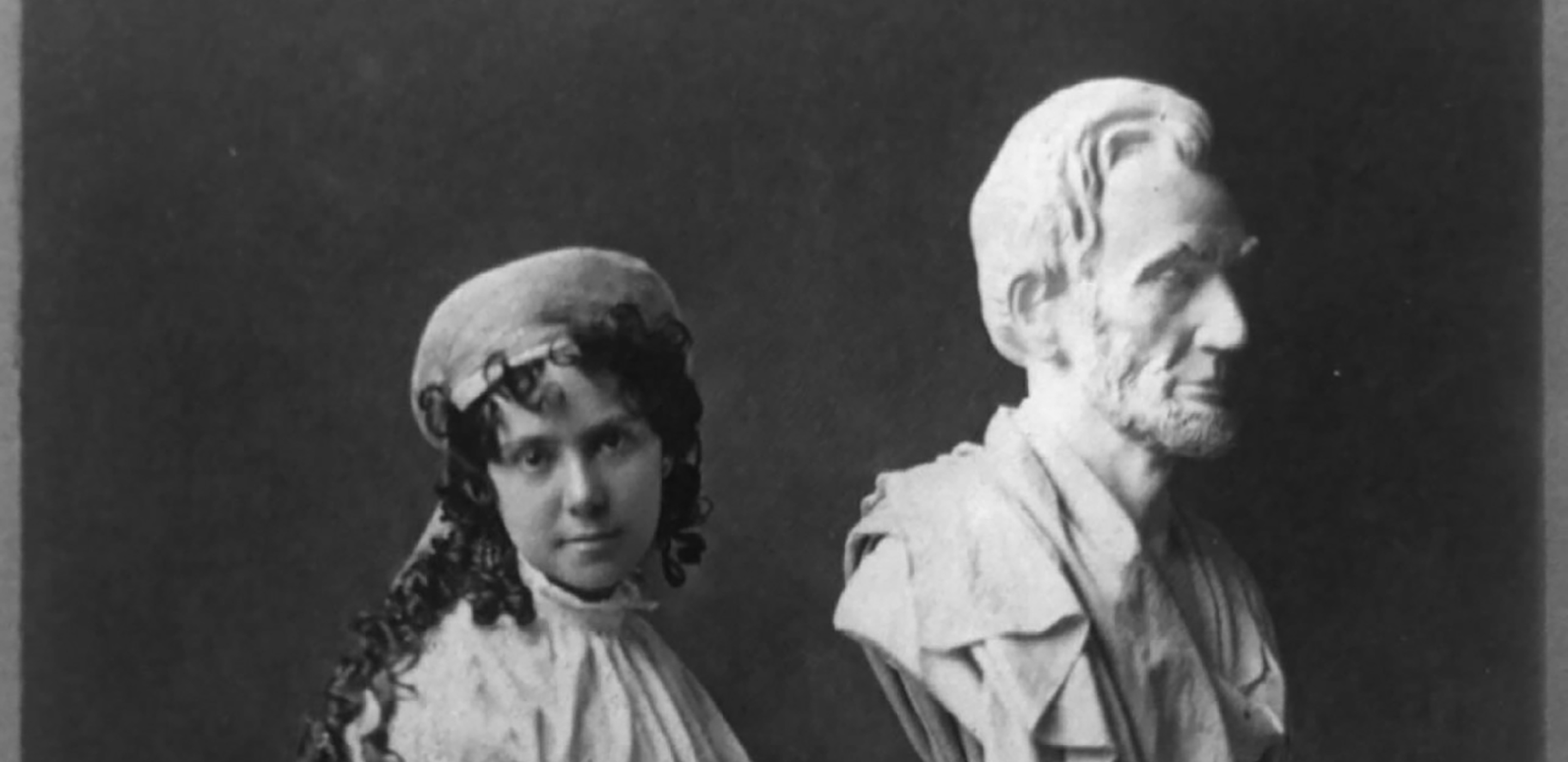Black and white photograph of a woman in a white gown next to a bust of Abraham Lincoln.