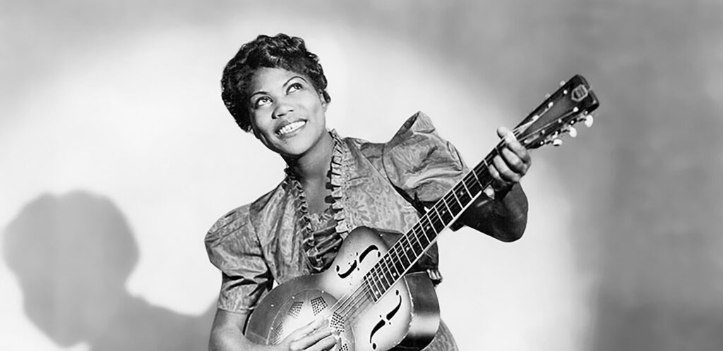 Black and white photograph of an African-American woman in a dress playing a guitar.