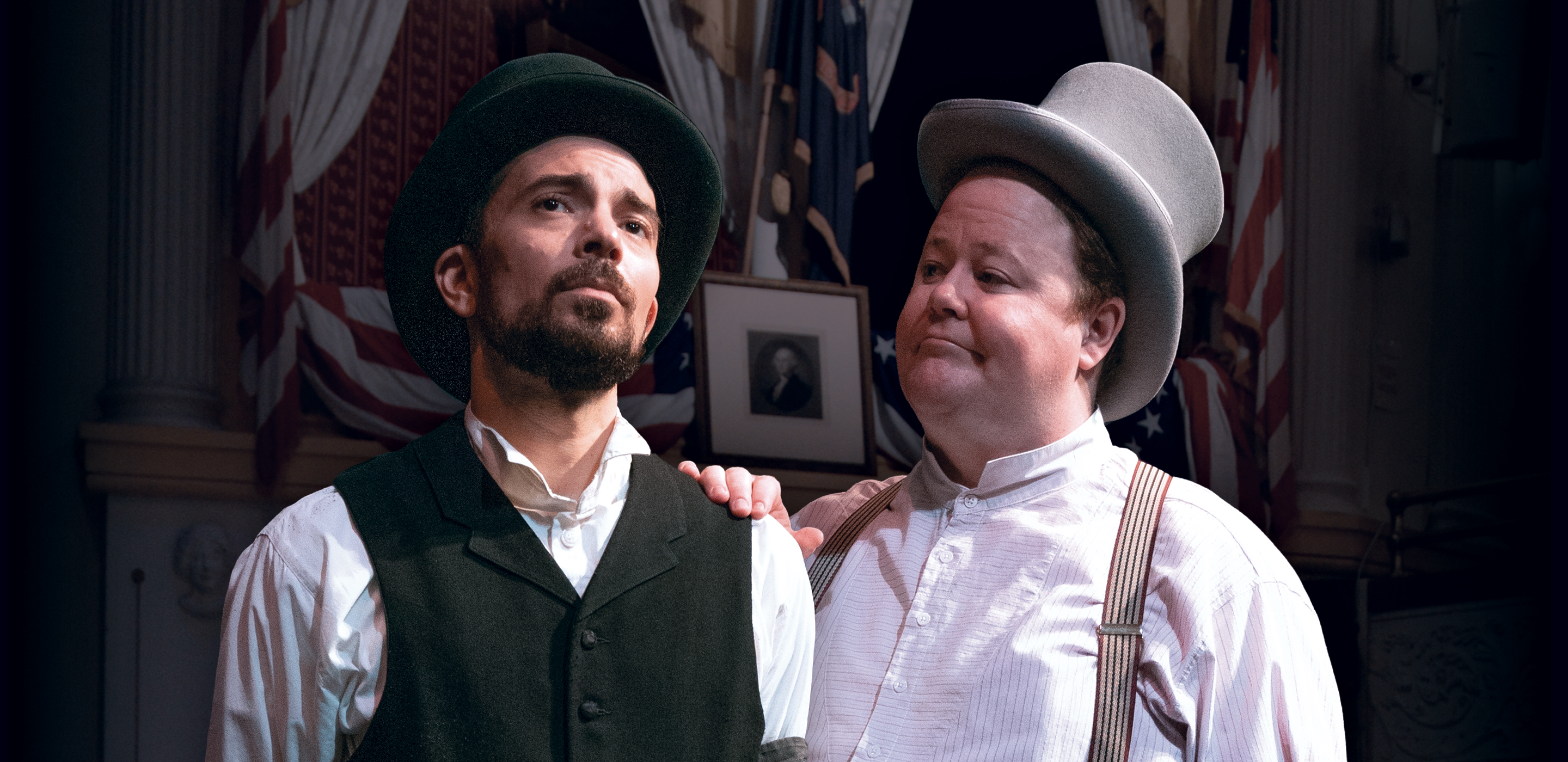 Actors playing Harry Ford and Harry Hawk wear 1860s costumes including top hats. They stand in front of the Ford’s Theatre Presidential Box.