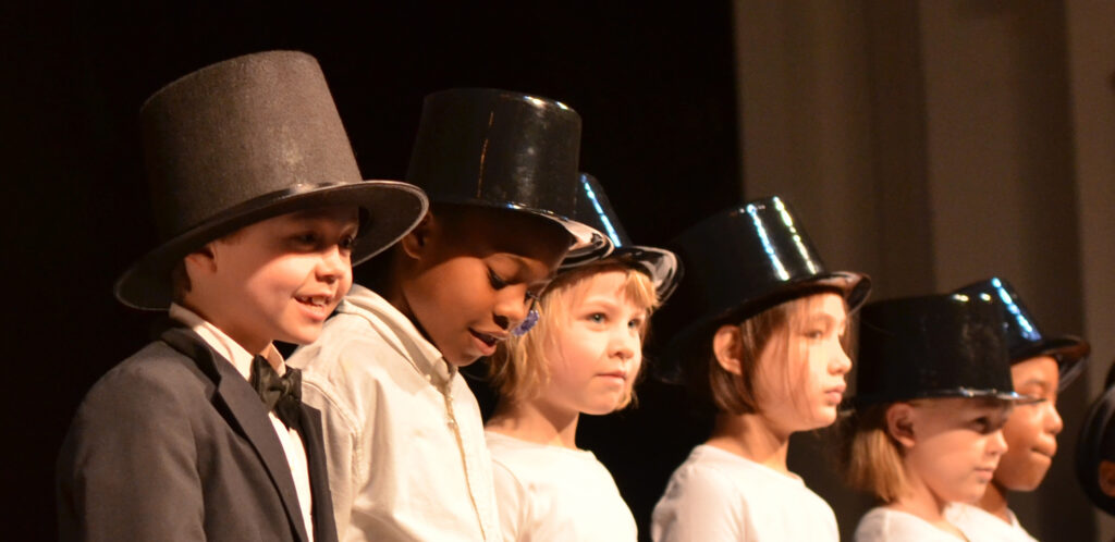 A row of children stand on the Ford's Theatre stage dressed in white shirts and stovepipe hats.