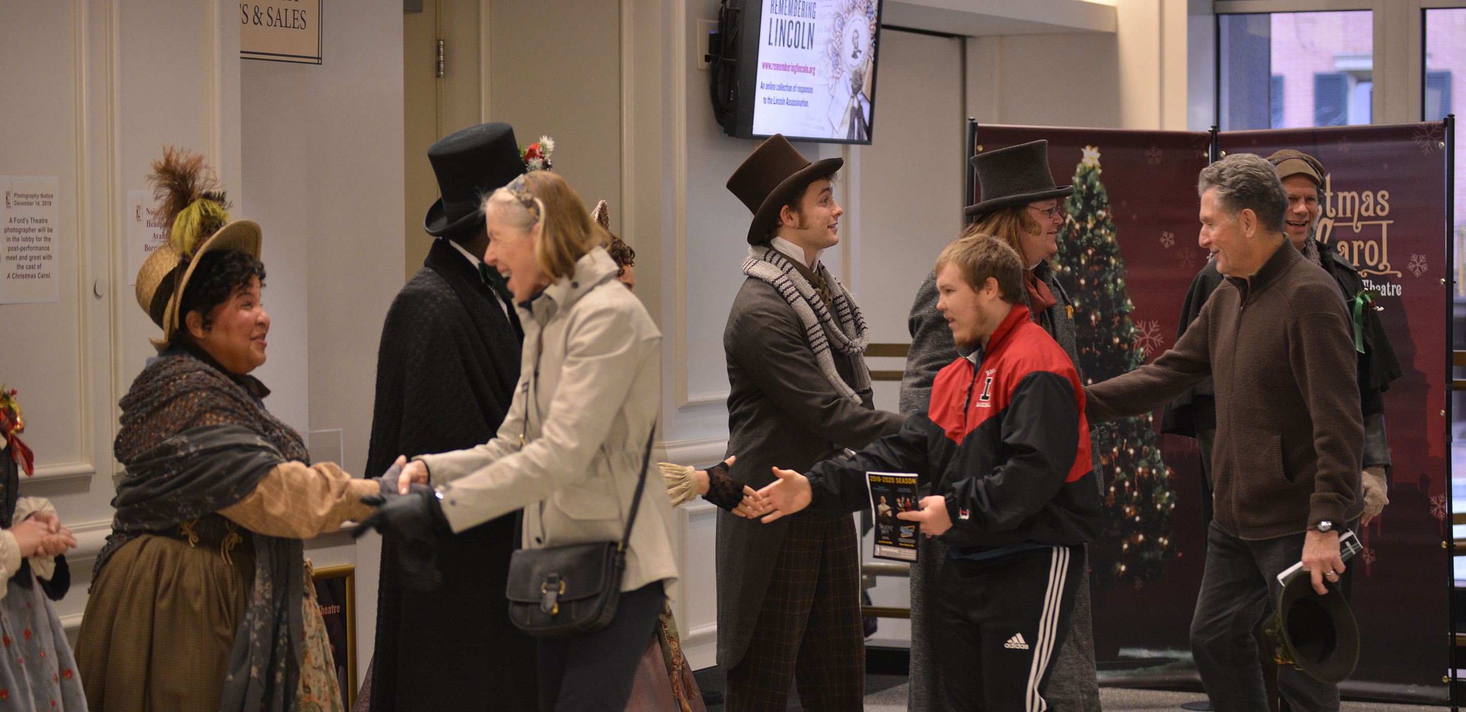 Three patrons shake hands with costumed actors as they walk through a receiving line.