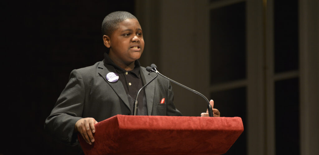 A young man stands at a podium and gives a speech.